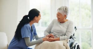 Caregiver smiling with elderly woman in wheelchair.